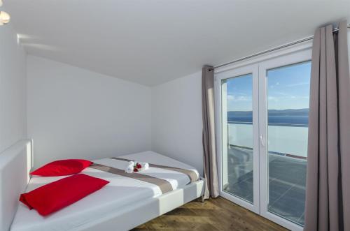 a white bed with red pillows in a room with a window at Apartments Lorenzo in Lokva Rogoznica
