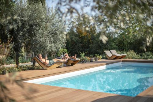 two people laying in lawn chairs next to a swimming pool at Le Mas des Romarins, FAYENCE in Fayence