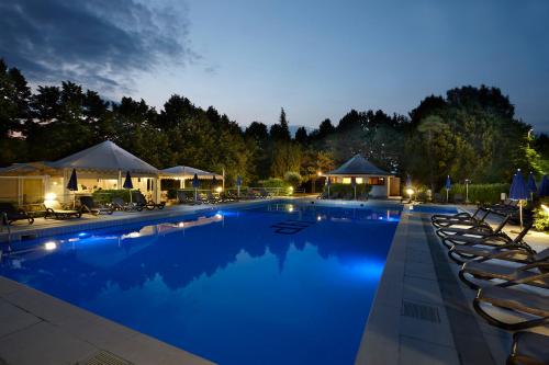 a large swimming pool with chairs and umbrellas at night at Hotel Villa Patriarca in Mirano