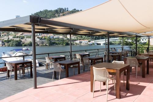 a patio with tables and chairs and a view of the water at Douro Hotel Porto Antigo in Cinfães