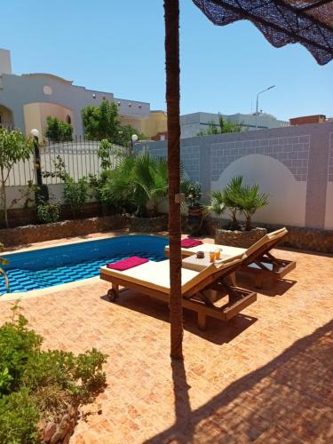 eine Terrasse mit einem Tisch und einem Sonnenschirm neben einem Pool in der Unterkunft Rum i villa med pool in Hurghada