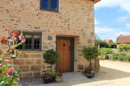 ein Steingebäude mit einer Holztür und ein paar Blumen in der Unterkunft Bramley Cottage at Stepps House in Broadway