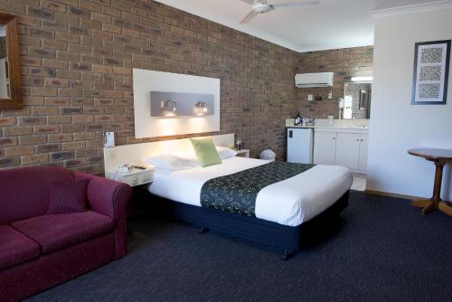 天鹅山Travellers Rest Motor Inn Swan Hill的一间卧室配有一张床、一把椅子和砖墙