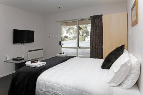 Un dormitorio con una gran cama blanca y una ventana en ASURE Amalfi Motor Lodge, en Christchurch