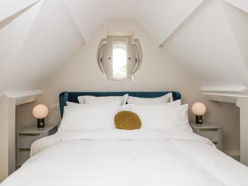 1 dormitorio con cama blanca y espejo redondo en The Hayloft, en Tetbury