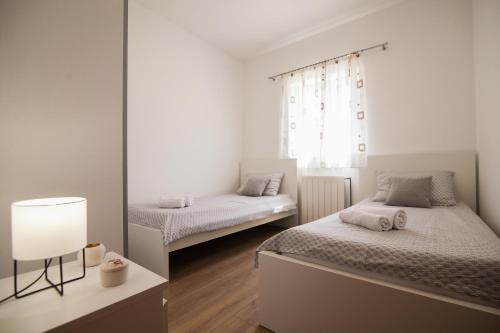 a white bedroom with two beds and a lamp at Apartments Teskera in Bol