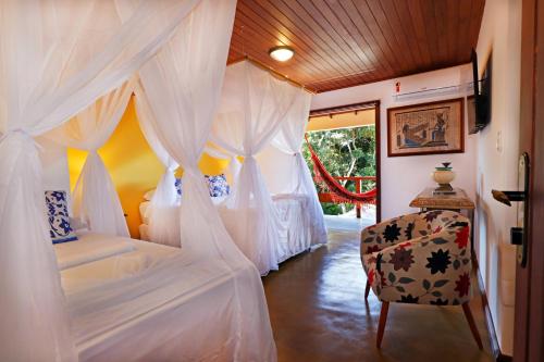 a bedroom with a bed with white drapes and a chair at Pousada Arraial Colonial, Localizada no Centrinho e de Fácil Acesso a Praia e a Rua Mucugê in Arraial d'Ajuda