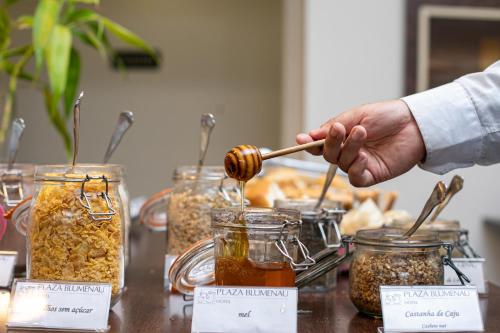 a person holding a honey spoon over jars of food at Plaza Blumenau Hotel in Blumenau