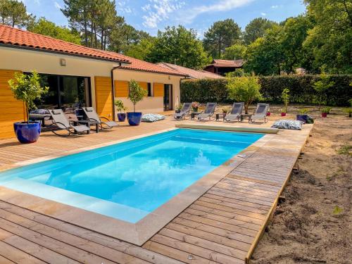 una piscina con una terraza de madera y sillas alrededor en Magnifique villa avec piscine, en Biscarrosse