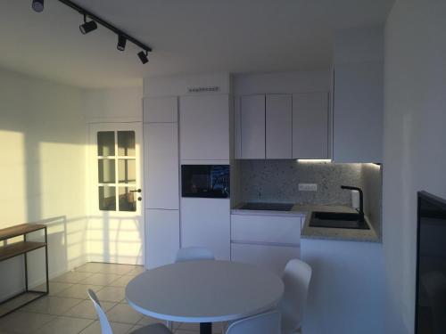 een witte keuken met een tafel en een wastafel bij Studio 4 pers met Frontaal Zeezicht & privé zwembad Oostende in Oostende