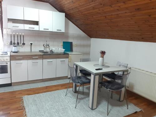 cocina con armarios blancos, mesa y sillas en Apartman Ljiljan, en Niš