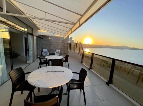 a balcony with tables and chairs and a view of the water at Cobertura Quebec Beira-Mar in Balneário Camboriú