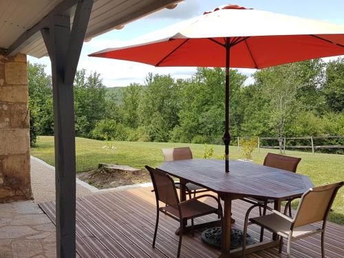 a wooden table with a red umbrella on a deck at Maison périgourdine avec jacuzzi, jardin privé et vélos - Idéal 2 personnes, près de Sarlat - FR-1-616-209 in Le Bugue