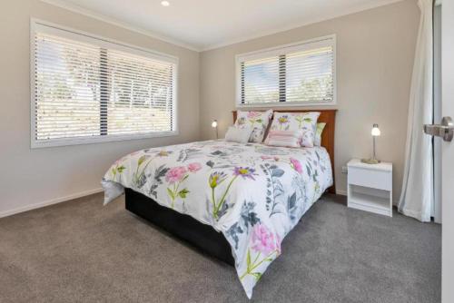 a bedroom with a bed with a floral bedspread and two windows at TuiRidge Tutukaka in Tutukaka