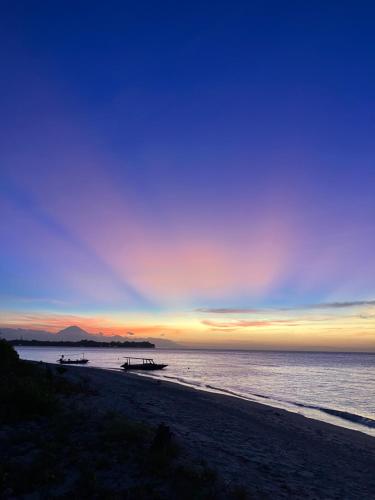una puesta de sol en una playa con barcos en el agua en Meno Madia Bungalows, en Gili Meno
