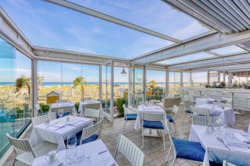 a restaurant with white tables and chairs and windows at Hotel Astoria in Caorle