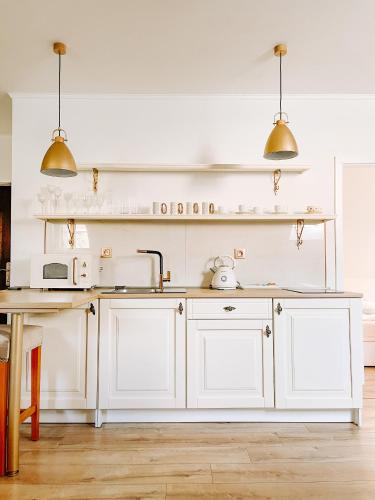 a kitchen with white cabinets and a sink and two lights at Apartmán Opera Prosecco Bar in Banská Štiavnica