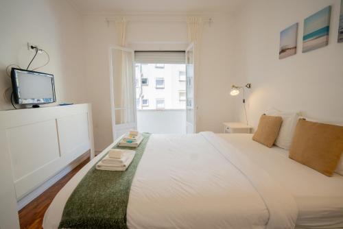 um quarto branco com uma cama grande e uma televisão em The Av. Roma Apartment em Lisboa
