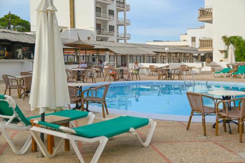 een zwembad met stoelen en tafels en een parasol bij Hotel Pinos Playa in Cala Santanyi