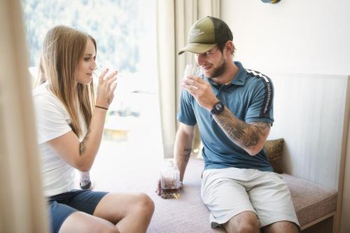 a man and a woman sitting on a couch drinking wine at Hotel Die Arlbergerin - Design & Tiroler Gemütlichkeit in Sankt Anton am Arlberg