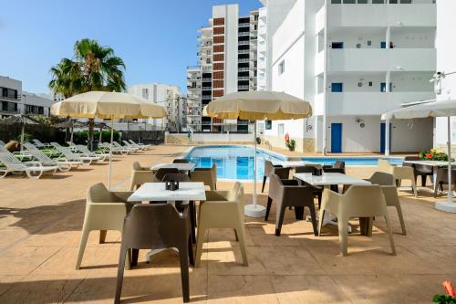eine Gruppe von Tischen und Stühlen mit Sonnenschirmen neben einem Pool in der Unterkunft Hotel Apartamentos Vibra Central City - Adults only in Sant Antoni de Portmany