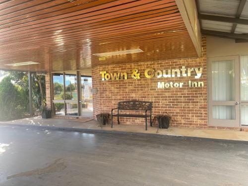 un banco frente a un edificio con un cartel en Town & Country Motor Inn en Forbes