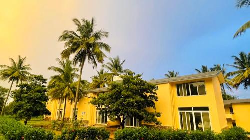 a yellow building with palm trees in front of it at Commune18 Resort Chikmagalur in Chikmagalūr