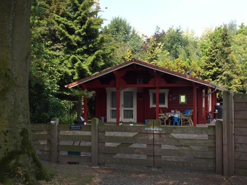 a red cabin in the woods behind a fence at Vakantiewoning Hegga in Hegelsom
