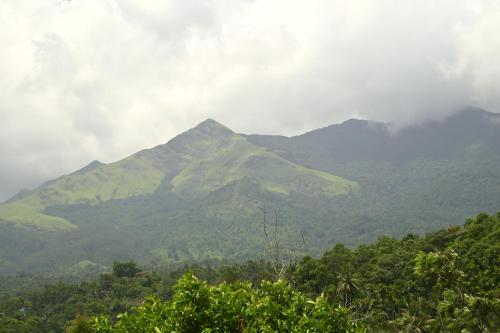 a mountain in the distance with clouds and trees at Besrauma Vythiri in Vythiri
