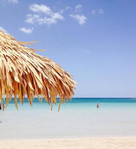 a straw umbrella on a beach with people in the water at Conchiglia Azzurra Resort & Beach in Porto Cesareo
