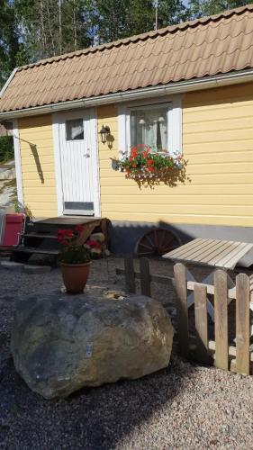 a house with a bench and a rock in front of it at Sjönära liten stuga med sovloft, toilet in separate small house, only OUTDOOR shower! in Åkersberga