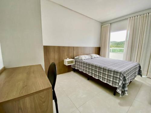 Un dormitorio con una cama y un escritorio y una ventana. en Apto 80m da Praia Grande vista mar!, en Governador Celso Ramos