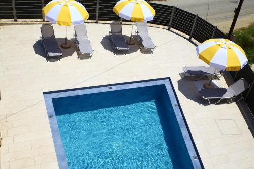einen Blick über einen Pool mit zwei Sonnenschirmen und Stühlen in der Unterkunft Armonia Rooms in Laganas