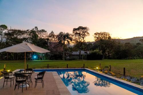 a pool with a table and chairs and an umbrella at Montanhas Do Visconde in Visconde De Maua