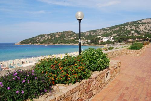 a stone wall with flowers and a street light next to the beach at Hotel Mon Repos in Baja Sardinia