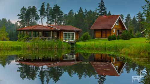 a cabin on the shore of a lake with its reflection in the water at Viesu mājas Briedīši in Raiskums