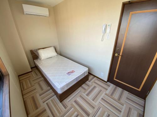 um pequeno quarto com uma cama e uma porta em lifeone club em Hiroshima