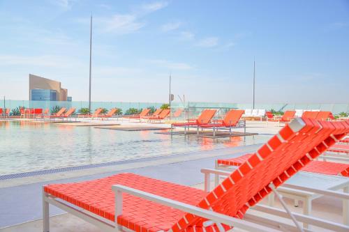 an empty swimming pool with orange chairs and water at The Bentley Luxury Hotel & Suites in Doha