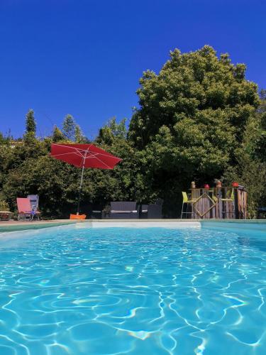 a swimming pool with a red umbrella and chairs at Gîte effet d’art in Saint-Privat