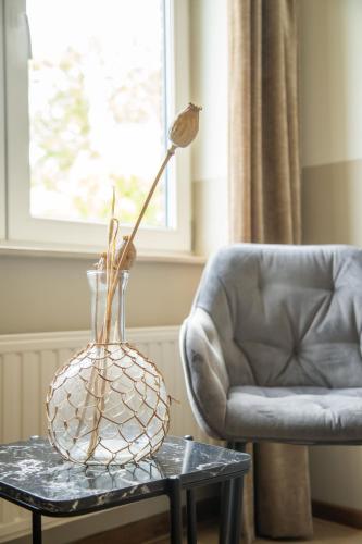 a glass vase with a flower on a table next to a chair at Blauwe Hoeve Luxe, ruimte, privacy en rust in Retranchement