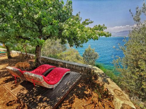 a red couch sitting under a tree next to the water at Ece Hotel Sovalye Island in Fethiye
