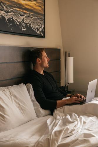 a man laying in bed using a laptop computer at Sundial Hotel in Whistler