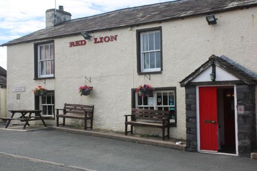 a building with two benches and a red door at The Red Lion in Lowick Green