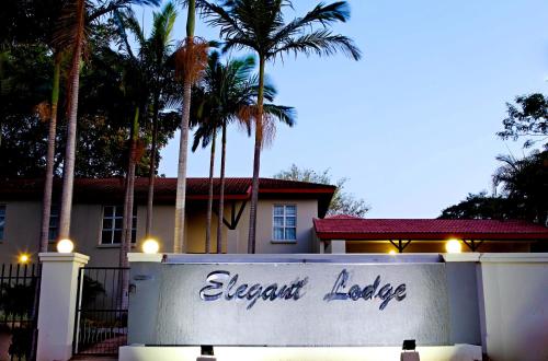 a sign in front of a house with palm trees at Elegant Lodge & Conference Center in Pongola