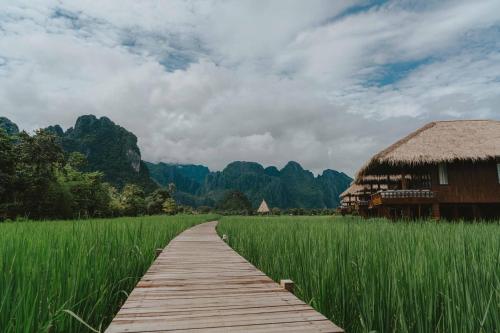 einen Holzweg durch ein Feld mit einer Hütte in der Unterkunft ViengTara VangVieng Resort in Vang Vieng