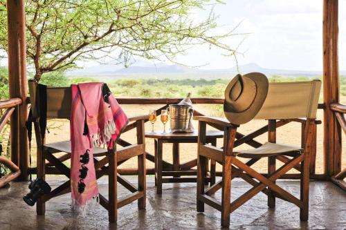 a table and chairs on a porch with a hat at Severin Safari Camp in Tsavo West National Park