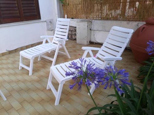 dos sillas blancas y flores púrpuras en un porche en La casa di Anna, en Patti