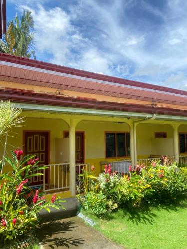 una casa amarilla con porche y algunas flores en Uptown Guesthouse en Siquijor