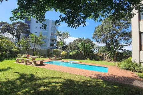 a swimming pool in a park with benches and a building at Juanita 202 Margate North Beach in Margate