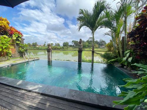 a swimming pool in front of a pond with palm trees at Sitala Villa in Ubud